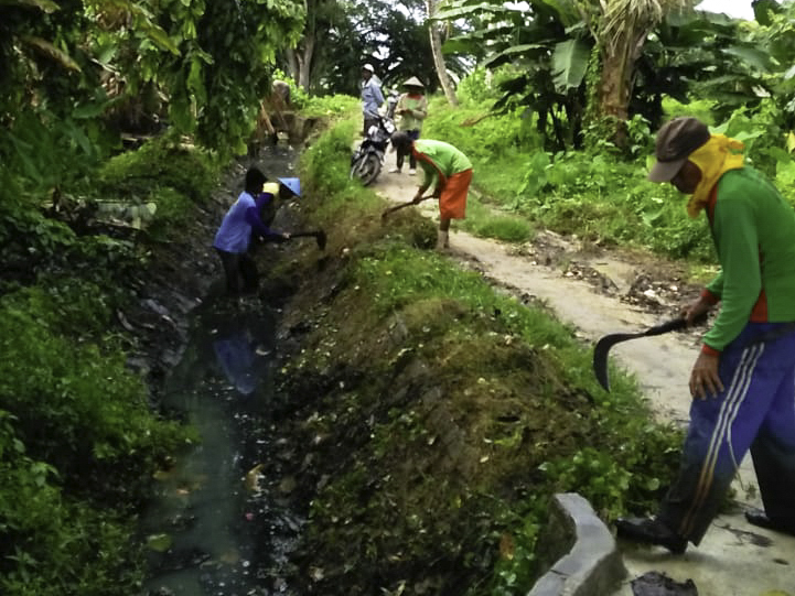 Workers clean an irrigation canal from overgrown vegetation, with funding from village funds